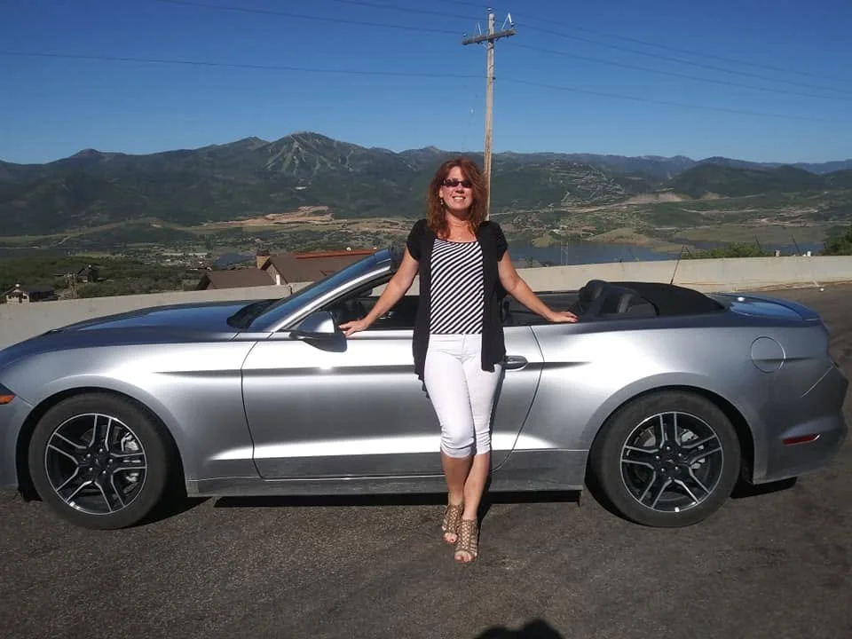Gina standing beside a silver convertible at Antelope Island State Park in Utah.