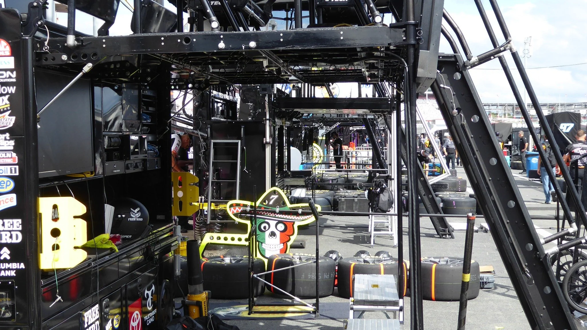 Panasonic Lumix ZS50 photograph showing NASCAR pit road equipment, stacked racing tires, team workstations, and the area behind the pit stalls.