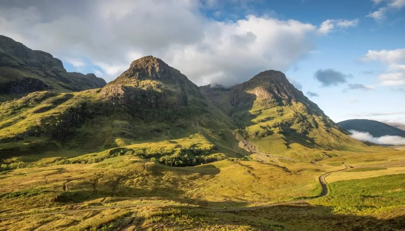 Sunlight breaking through the clouds across the green mountain landscape of Glencoe, Scotland.