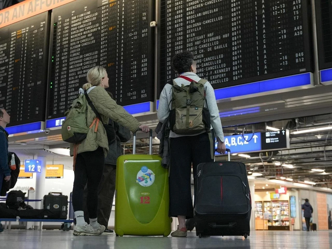 Travelers with luggage checking an airport departure board showing multiple canceled flights.