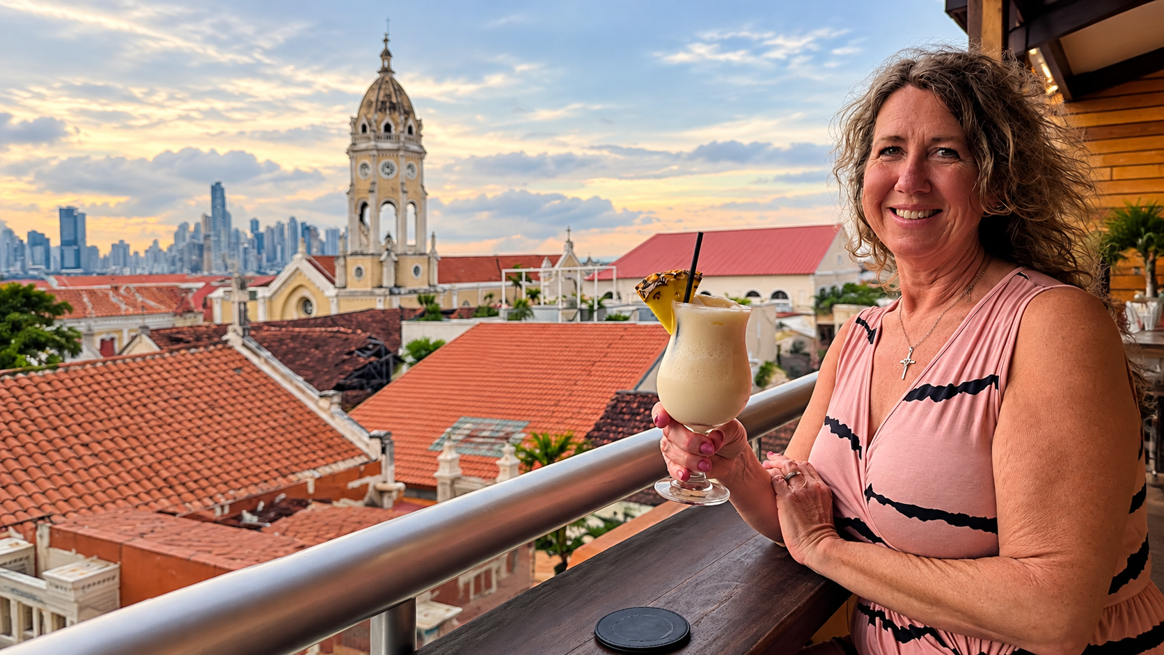 Woman enjoying a tropical cocktail at a rooftop bar overlooking the historic rooftops and church tower of Casco Viejo in Panama City.