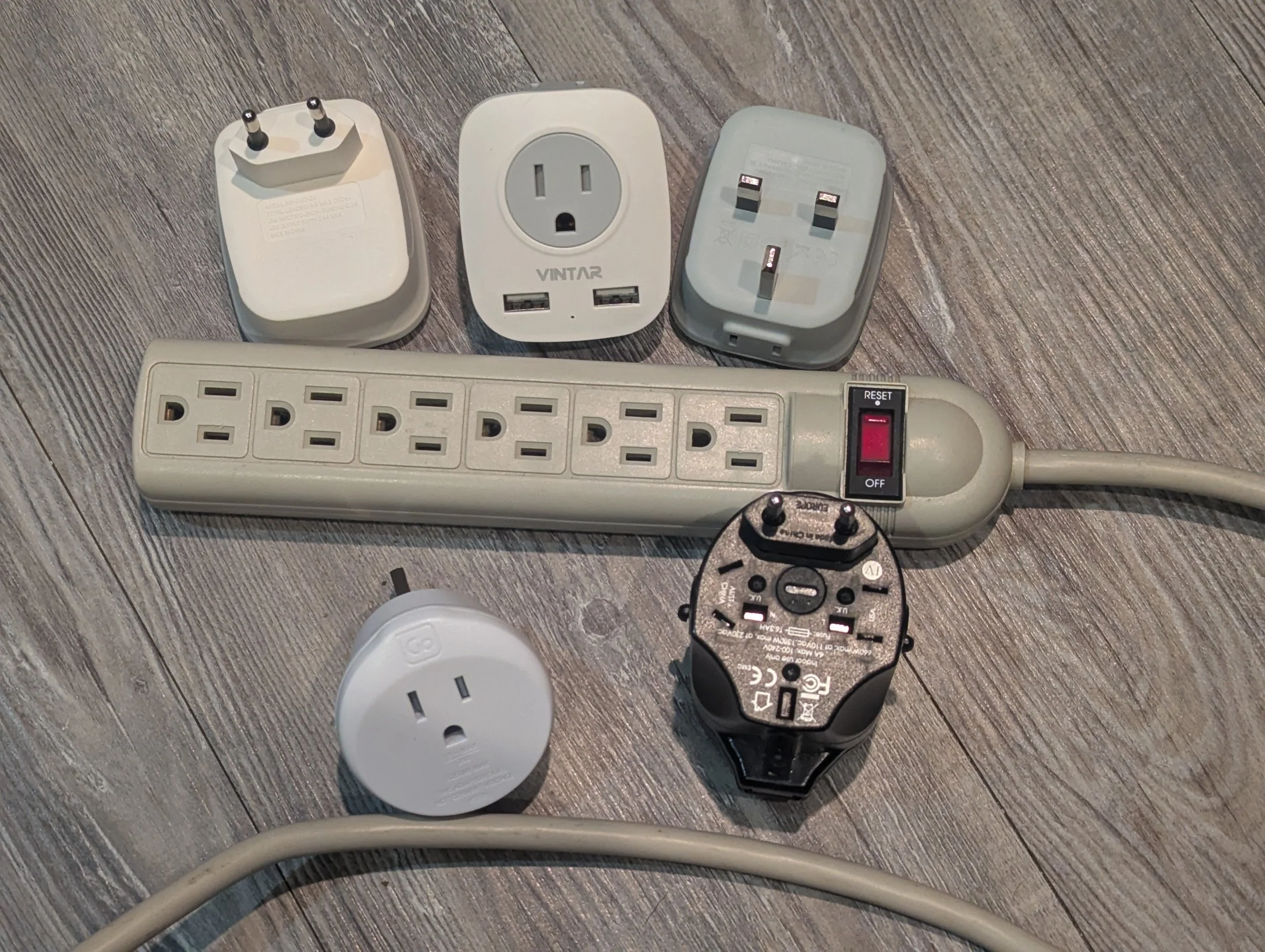 Collection of international travel adapters accumulated for trips to countries using different electrical outlet standards.