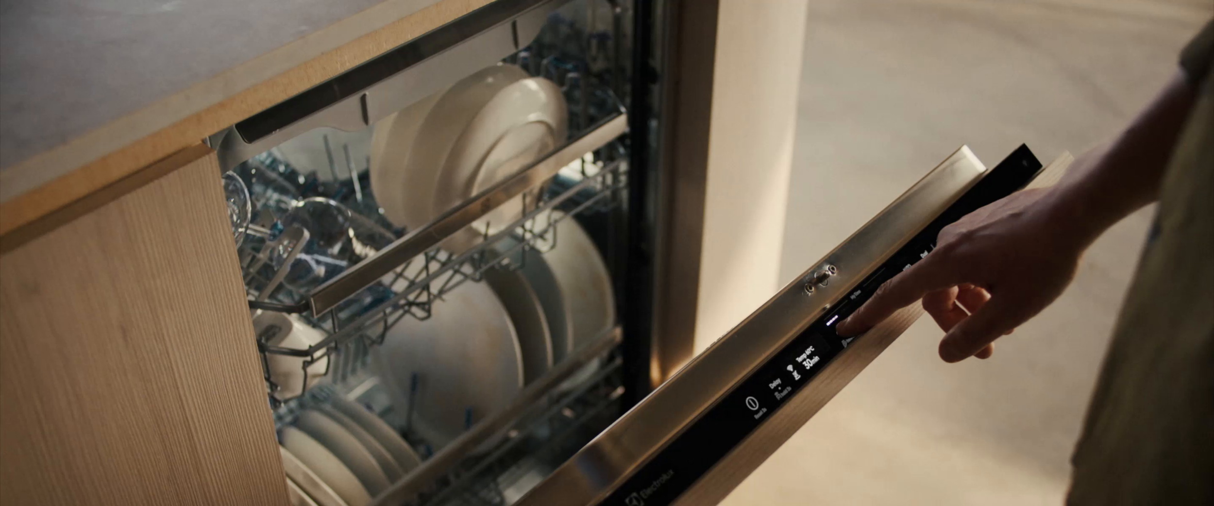 A person using a modern dishwasher to load or unload dishes, with the control panel visible.