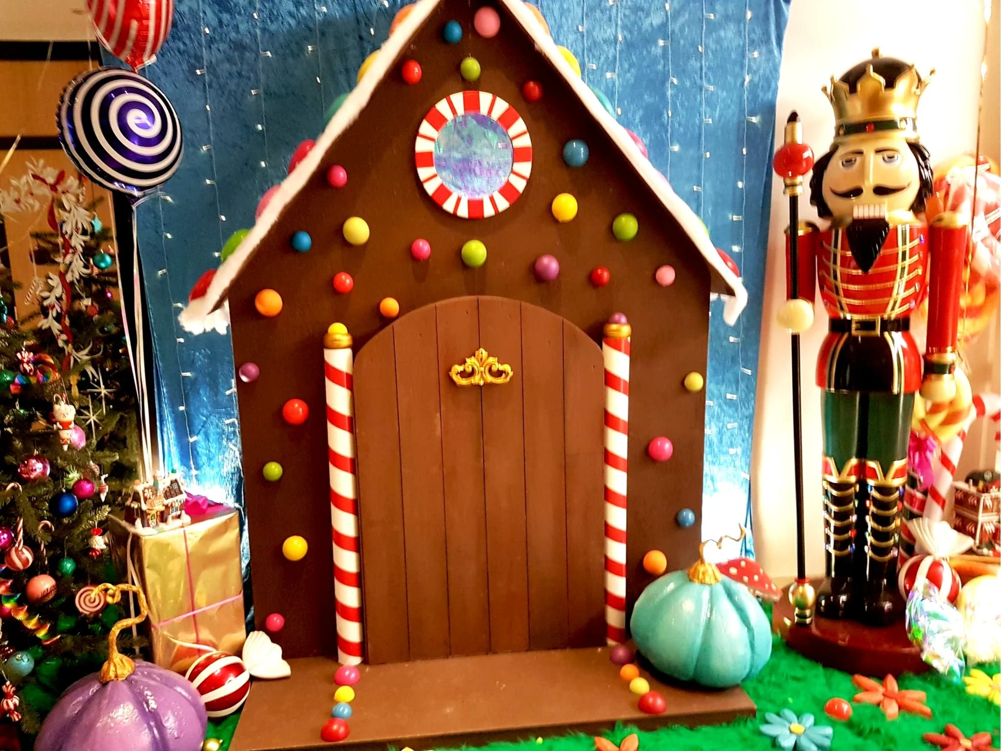  maison en pain d'épice décorée de bonbons colorés, avec un soldat en Nutcracker géant à côté, entourée de sapin de Noël et de décorations festives.