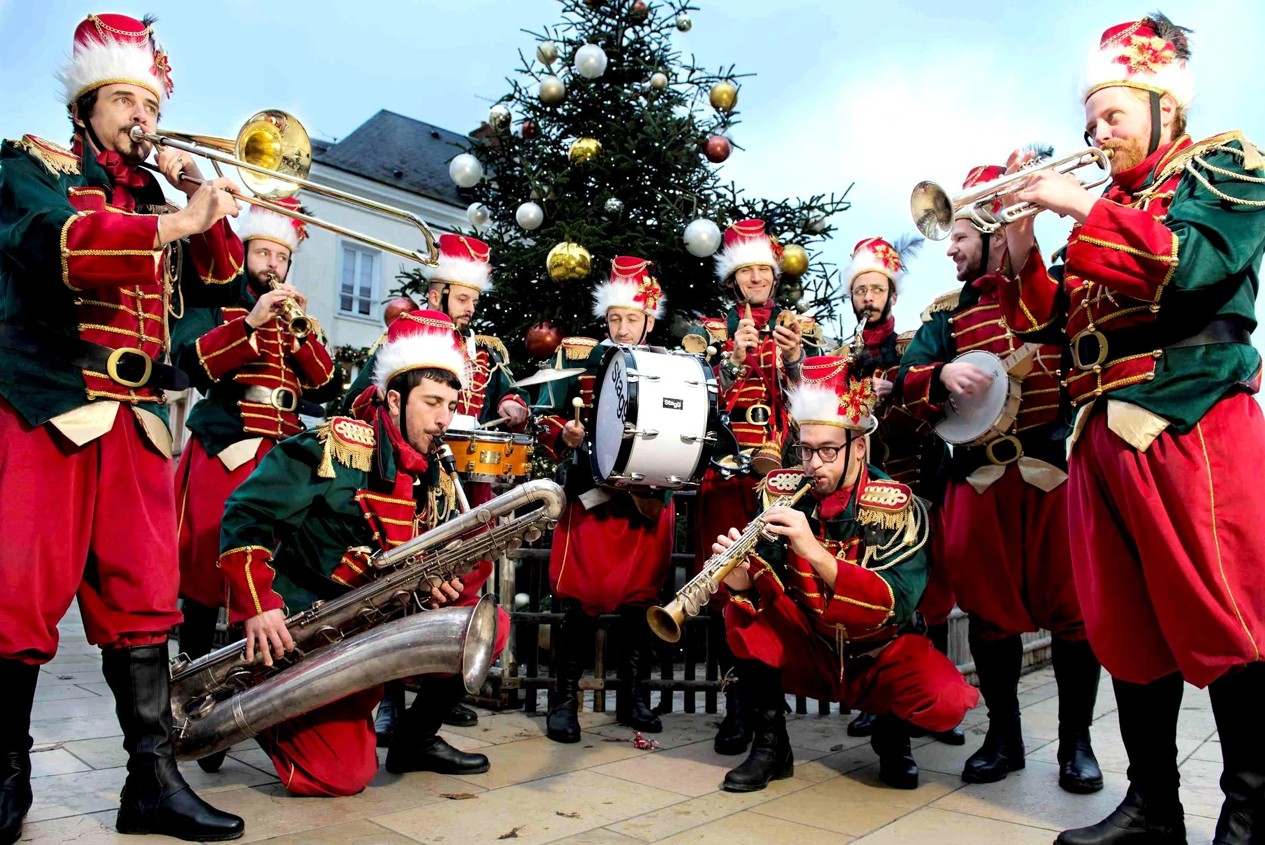 Groupe de musiciens habillés en costumes de Noël jouant de divers instruments devant un sapin décoré