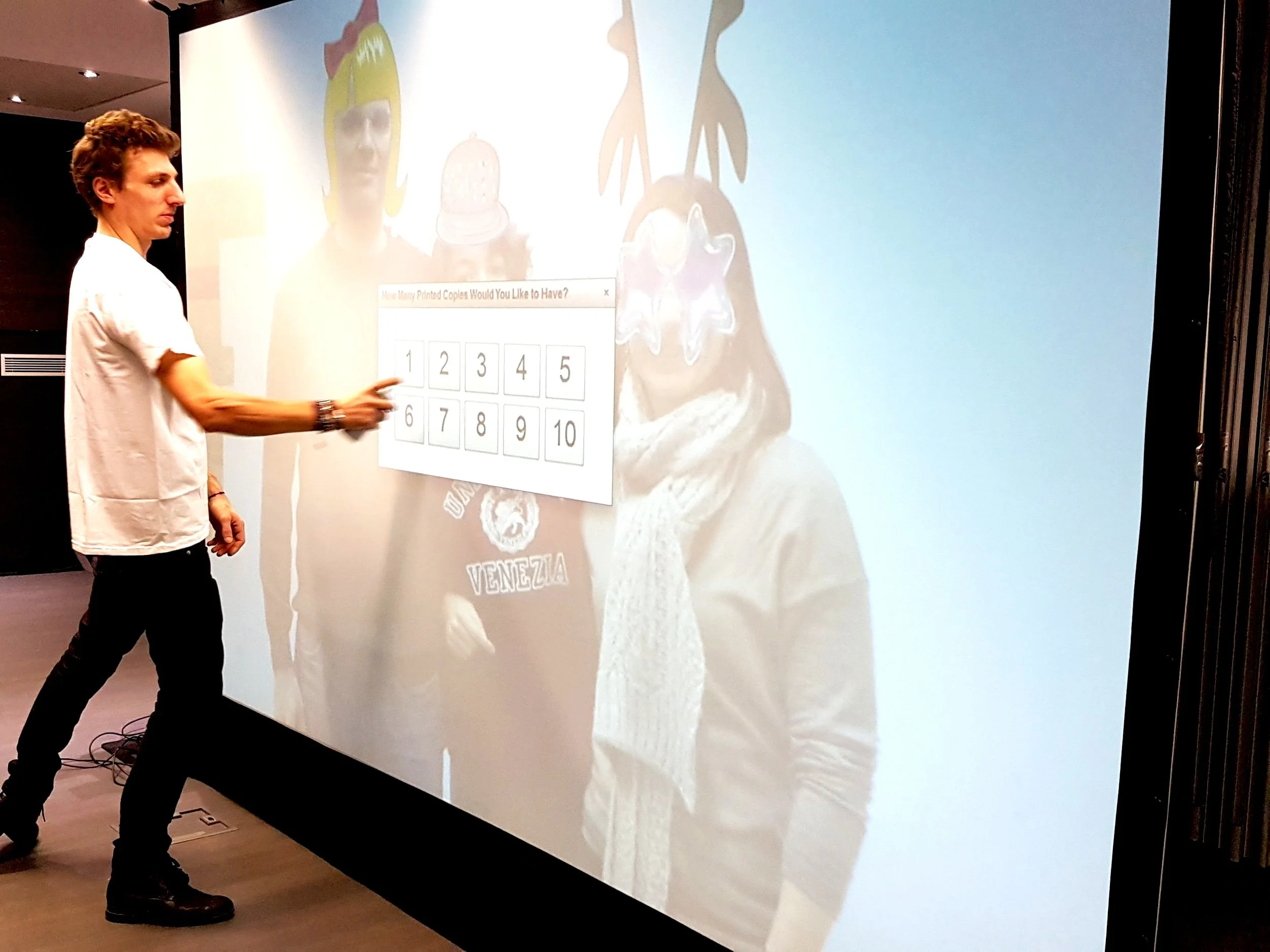 Un homme pointant un tableau interactif avec une fenêtre de sondage. En arrière-plan, une projection montre deux personnes portant des masques et un casque.