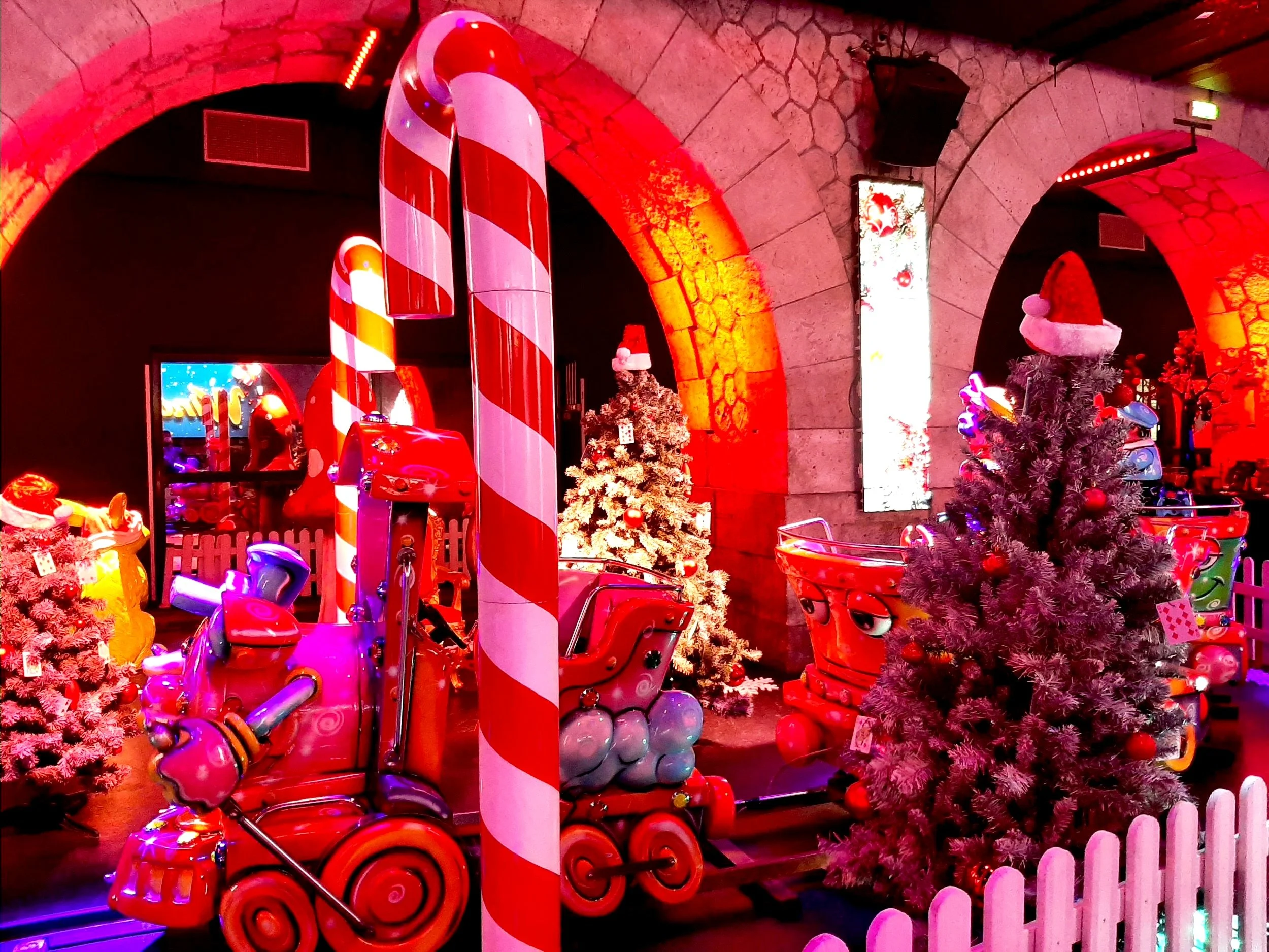 Décor de Noël avec des traîneaux, sapins de Noël, bonhommes de neige, et guirlandes lumineuses dans un espace festif.