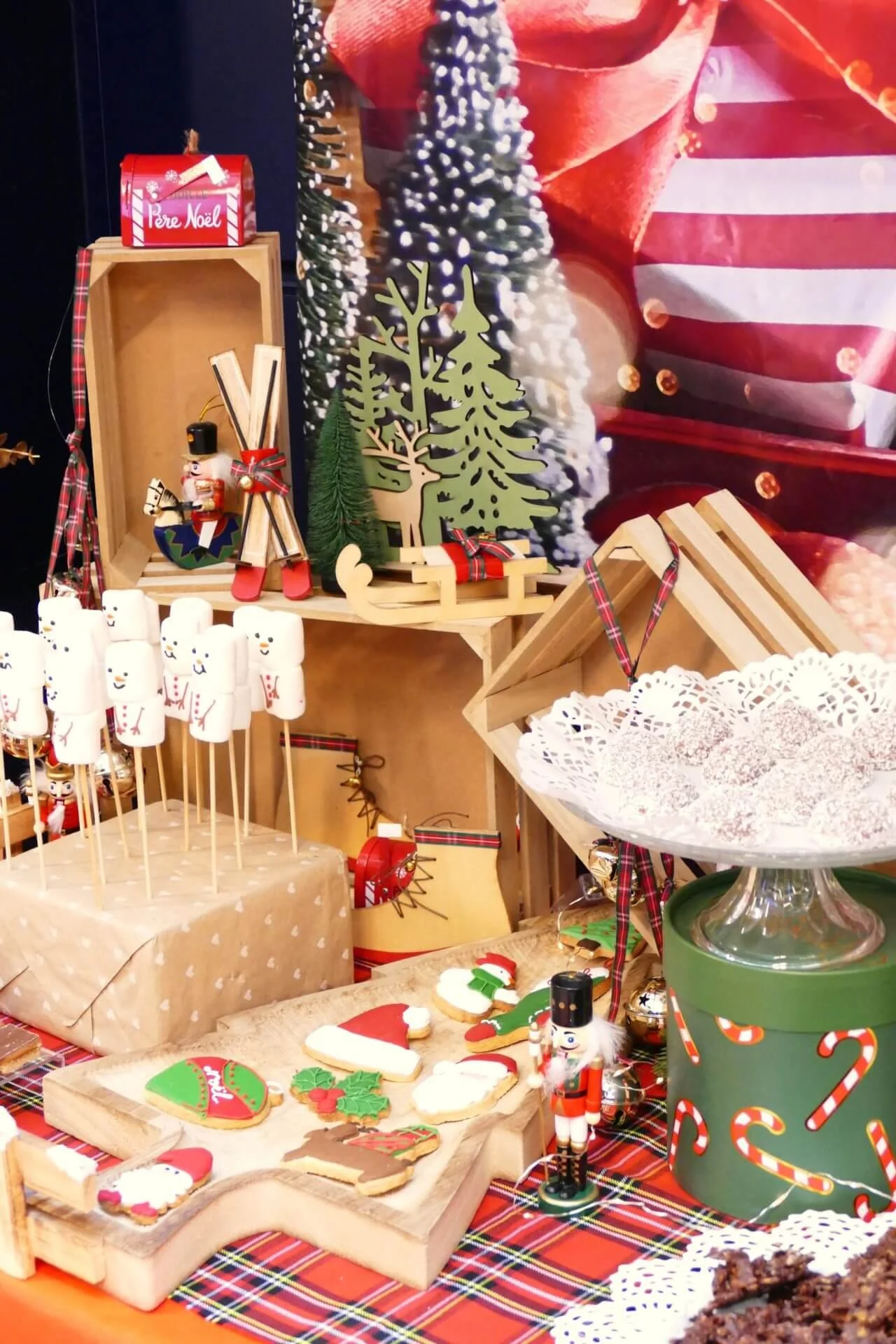 Décoration de Noël avec petits gâteaux, figurines de bonhommes de neige, sapins en bois, paniers, et alimentation festive.