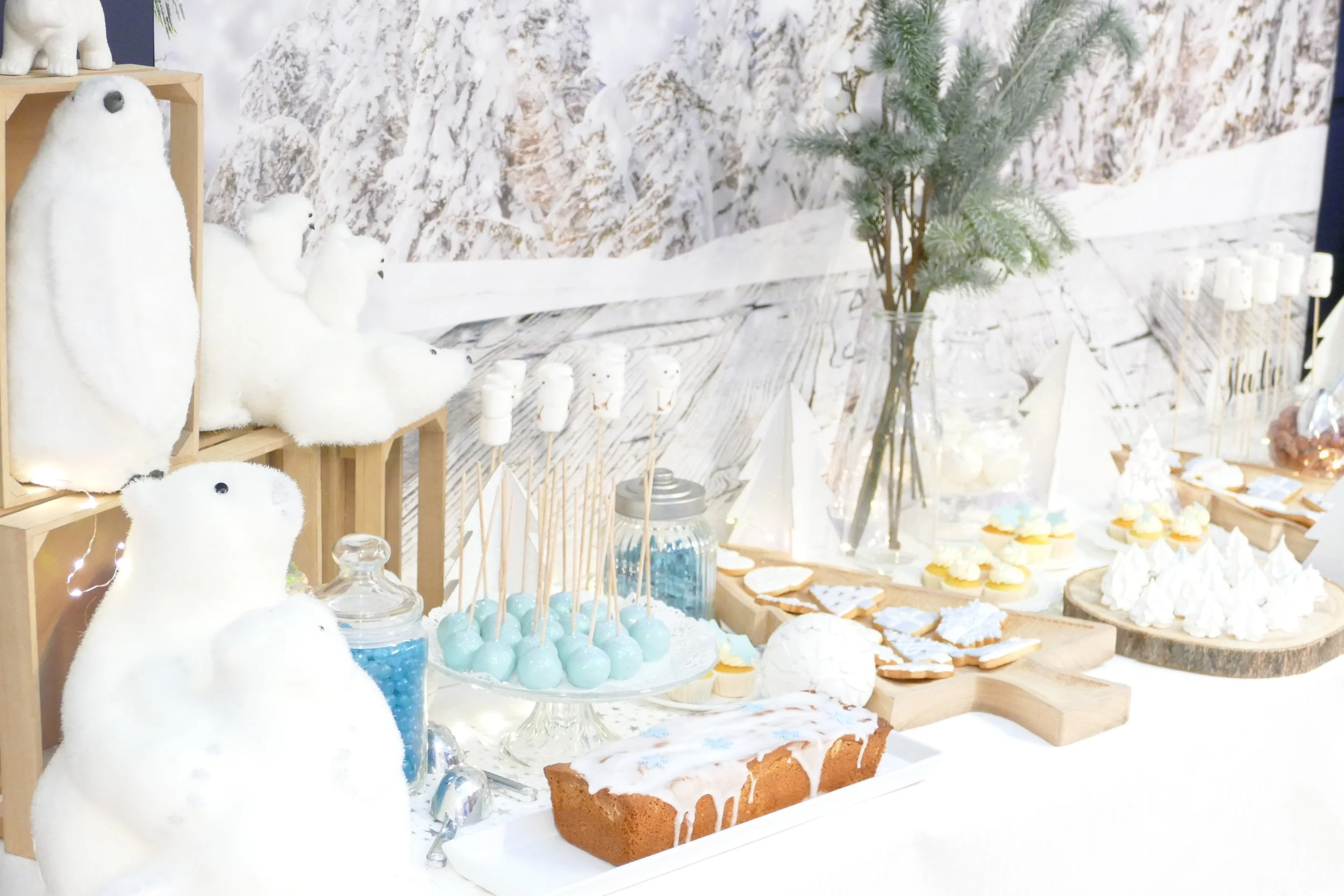 Décoration de fête d'hiver avec des ours en peluche, des bonbons bleus, des biscuits décorés, un gâteau, et des éléments de bois et de pin décorants.
