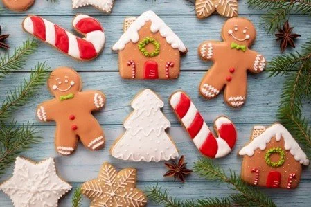 Gâteaux de biscuits de Noël en formes de bonhommes, maisons, étoiles de pain d'épice, cannes de sucre, branches de sapin, et étoiles en fond bleu clair.