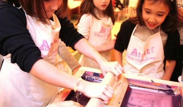 Des enfants, portants des tabliers, utilisent un rouleau pour fabriquer des pâtes.