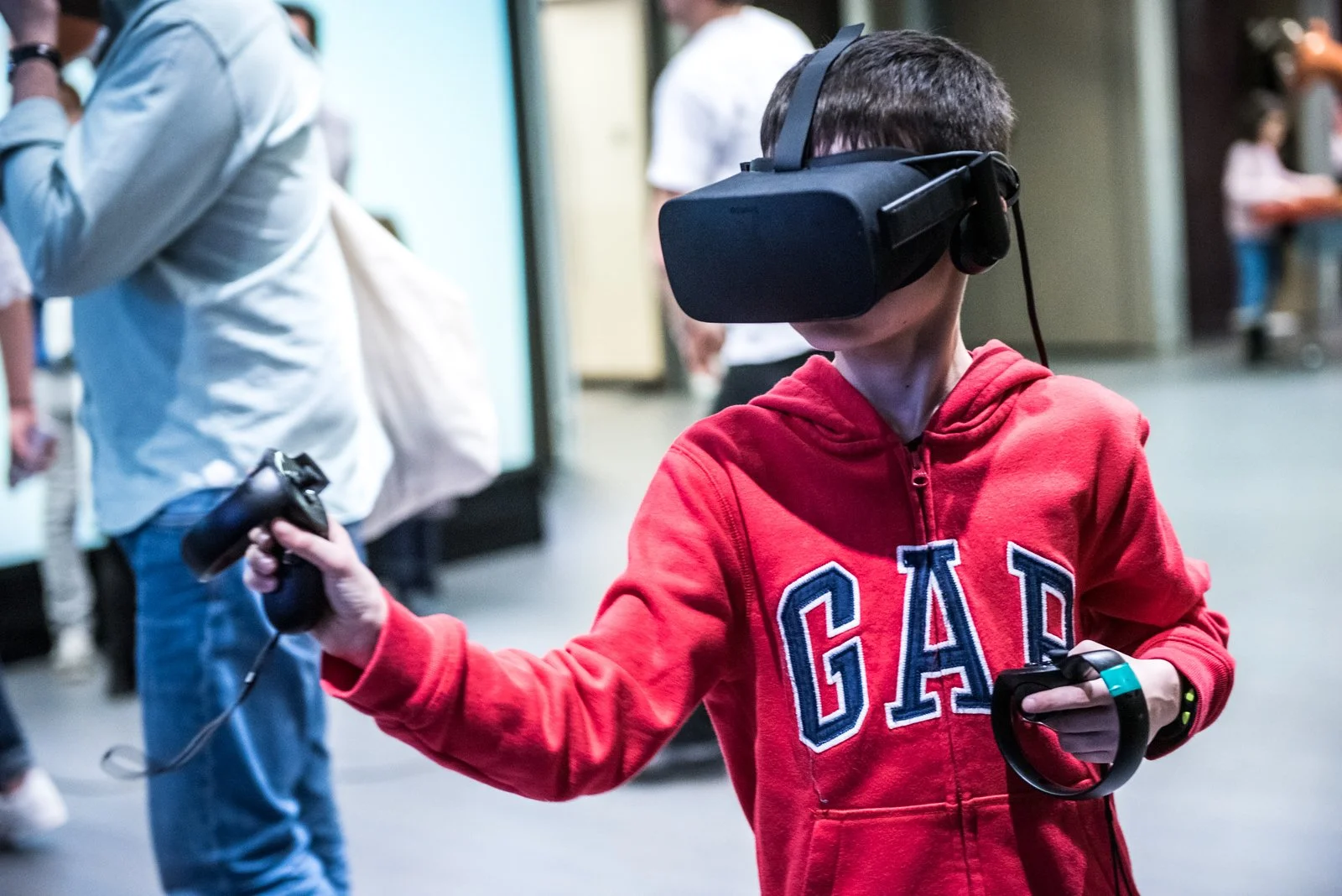 Un garçon portant un casque de réalité virtuelle avec une manette dans chaque main, dans un espace intérieur.