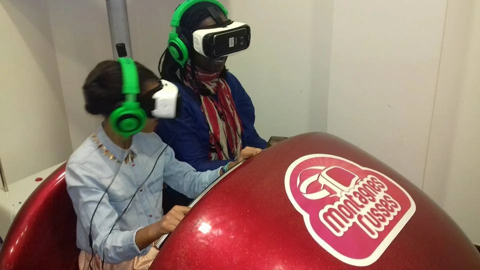 Deux personnes portant des casques de réalité virtuelle sont assises dans une capsule de jeu appelée Monstergardeuses Capsule.