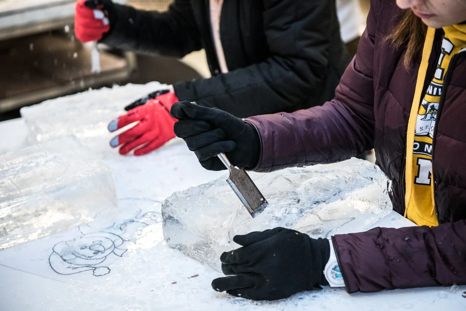 Deux personnes taillent un bloc de glace avec un couteau à glace.