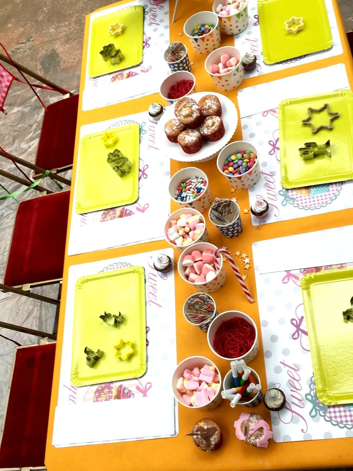 Table de fête pour enfants avec plats de cupcakes, bonbons, marshmallows, et décorations colorées.