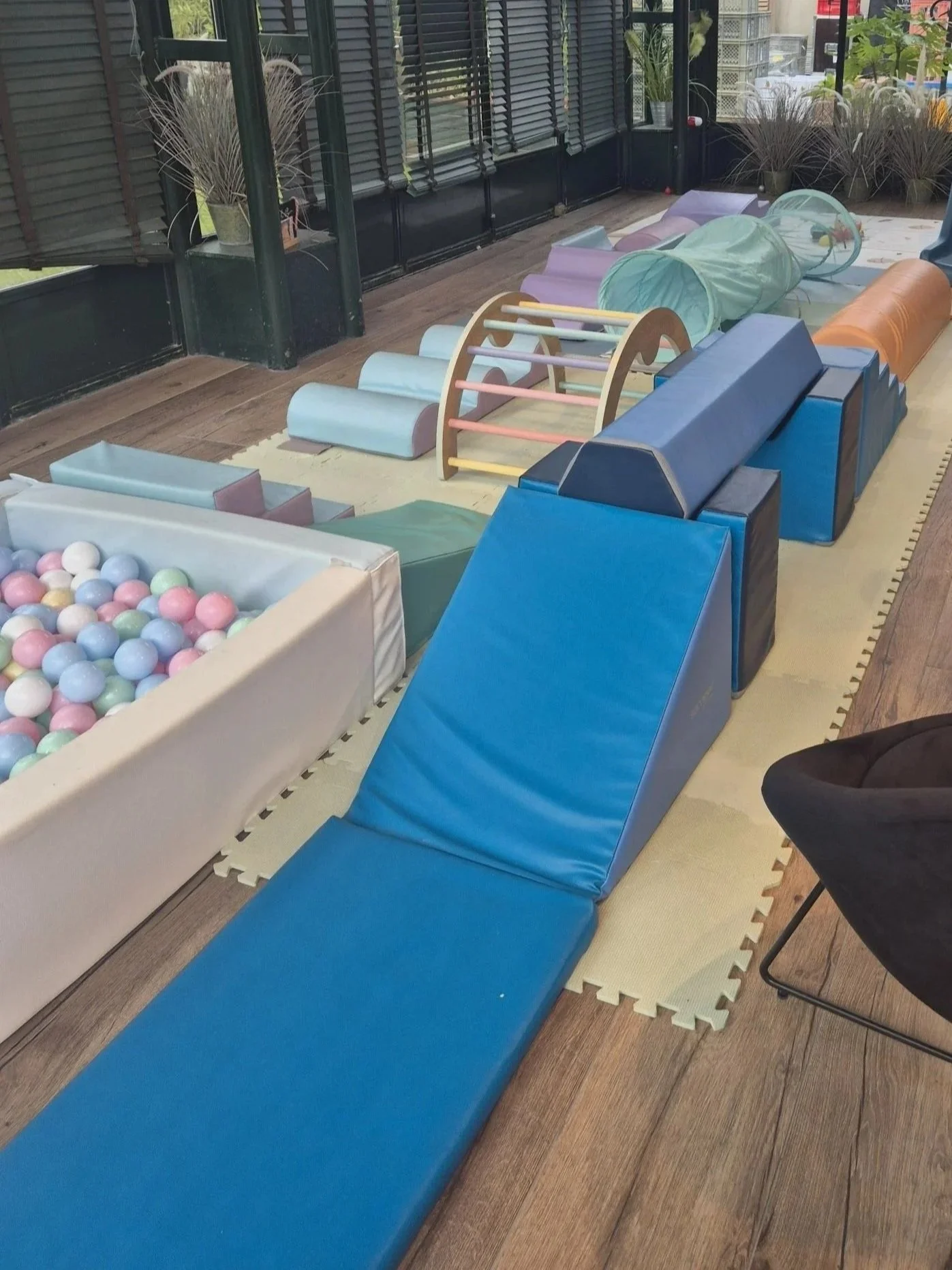 Espace de jeux pour enfants avec toboggans, tunnels, balles colorées, et tapis de jeu, dans une salle avec grandes fenêtres et décorations