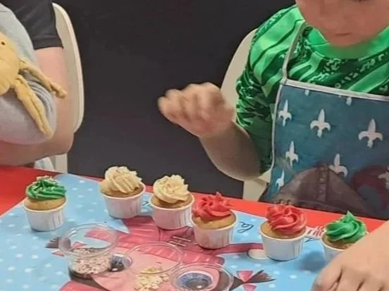Enfants regardant des cupcakes décorés, avec un garçon en vert et une fille en rose, sur une table avec un tapis de fête.atelier cupscakes agence kidsday 