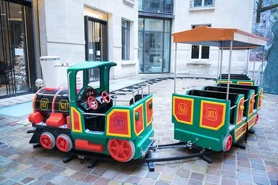 Petite locomotive de train électrique pour enfants avec wagon, en extérieur sur pavé, avec parasol