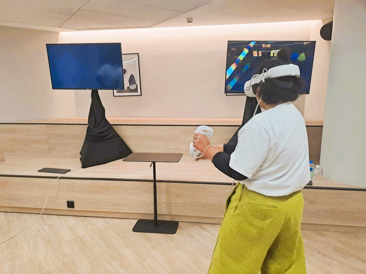 Une personne portant un casque de réalité virtuelle joue à un jeu vidéo avec deux écrans dans une pièce.
