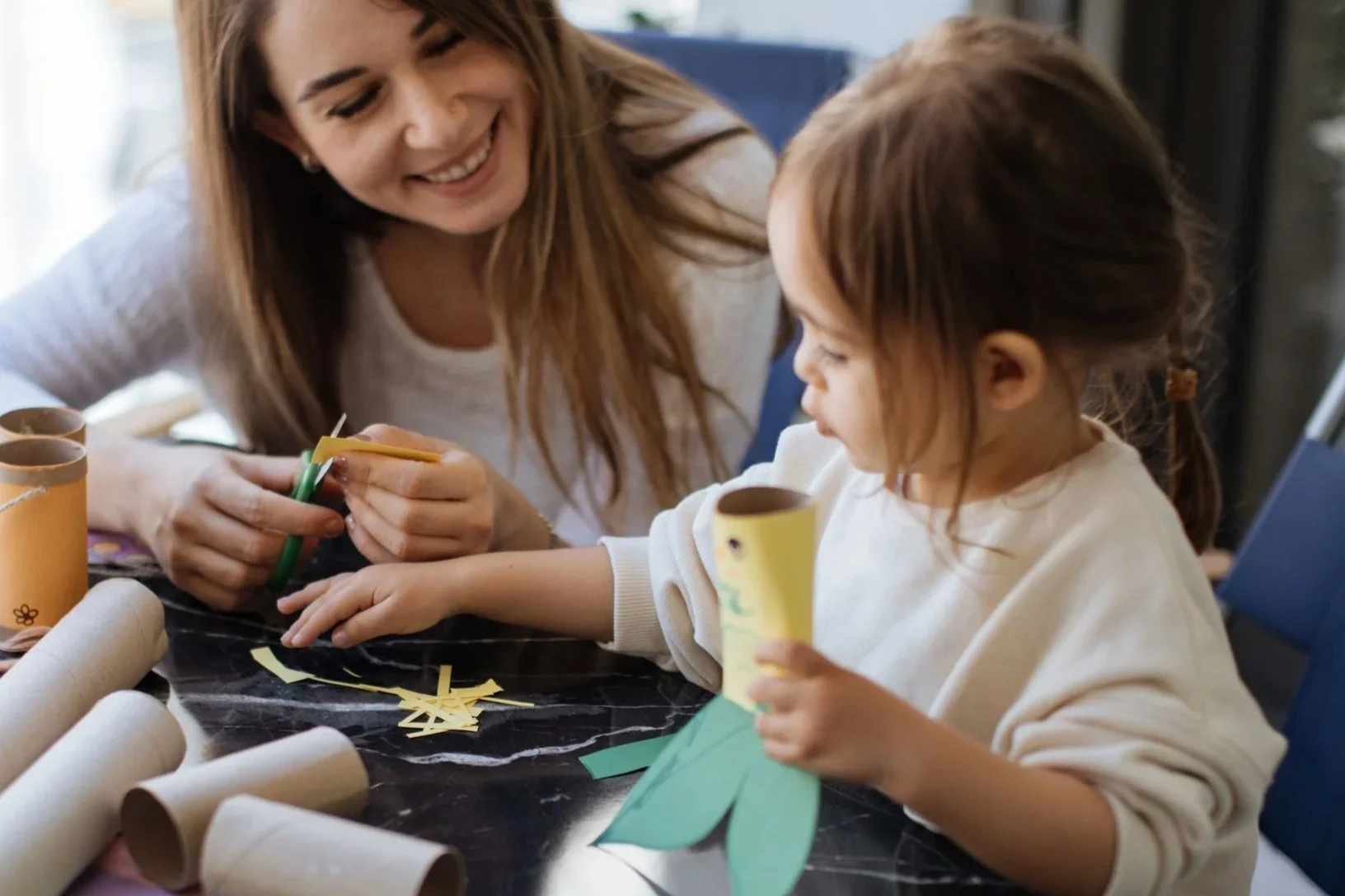 Une femme et une jeune fille colorient et découpent du papier pour un projet artistique artisanal assises à une table.