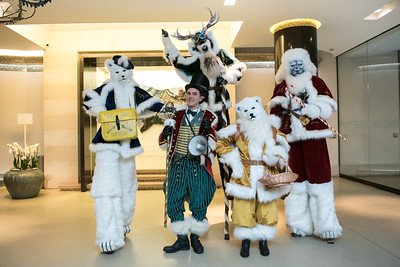 Groupe de personnes déguisées en personnages de Noël, dont deux en costumes d'animaux, dans un hall lumineux.