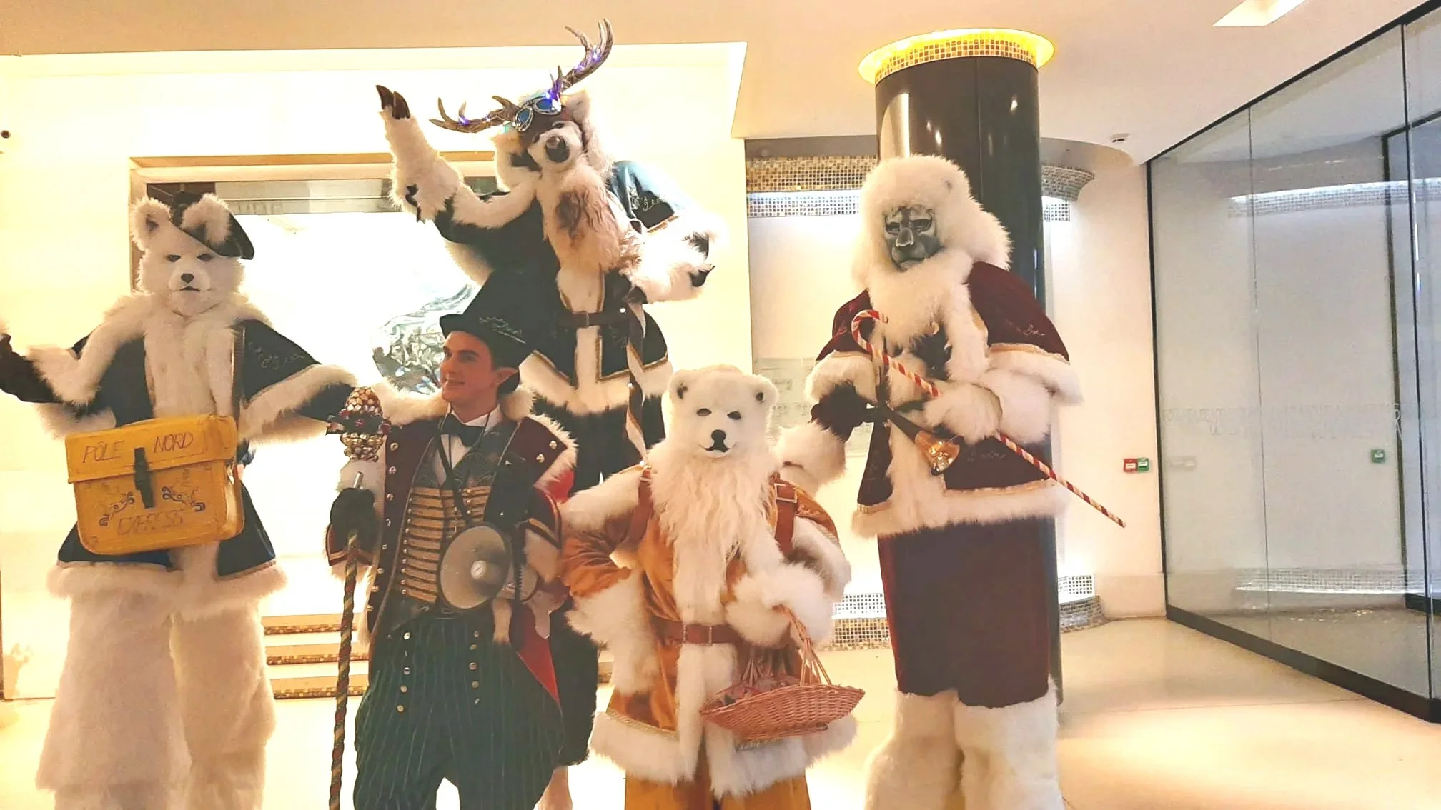 Personnes en costumes d'ours polaires, puces, et cerfs lors d'une animation ou d'une fête dans une zone intérieure.