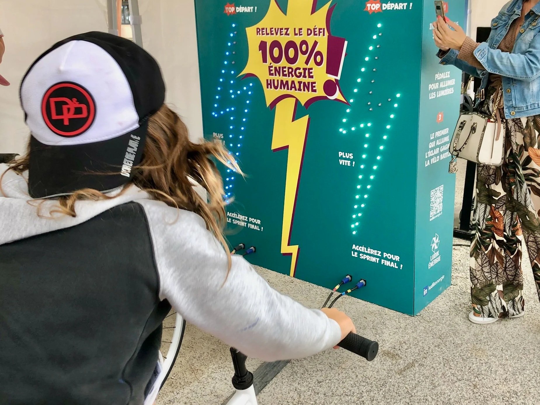 Une personne en fauteuil roulant joue à un jeu interactif énergique avec des lumières, comportant des instructions pour accélérer lors d'un sprint final, sur fond d'affiche jaune et bleue avec une foudre.
