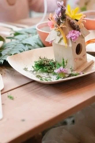 Pot de fleurs décoré avec un motif de soleil, une figurine de lapin en céramique blanche avec une carotte en plastique orange, et un tableau noir avec écriture en français "Atelier Petits pots".