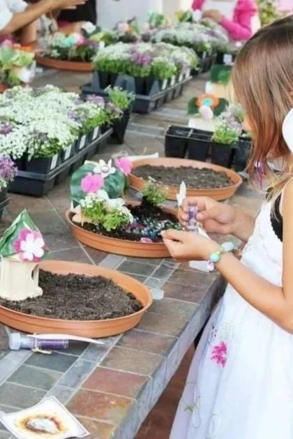 Une enfant participe à une activité de jardinage ou de décoration de petits pots avec des fleurs en pot, dans un espace en intérieur.