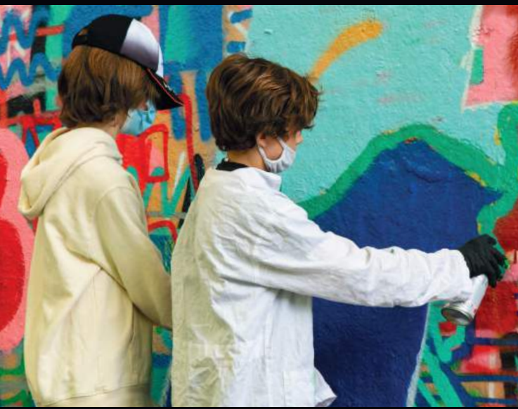 Deux jeunes en train de peindre un mur avec des graffitis, portant des masques et des gants.