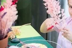 Deux personnes manipulant des plantes ou des fleurs en plastique ou séchées sur une table verte, avec des bouquets de fleurs en arrière-plan.