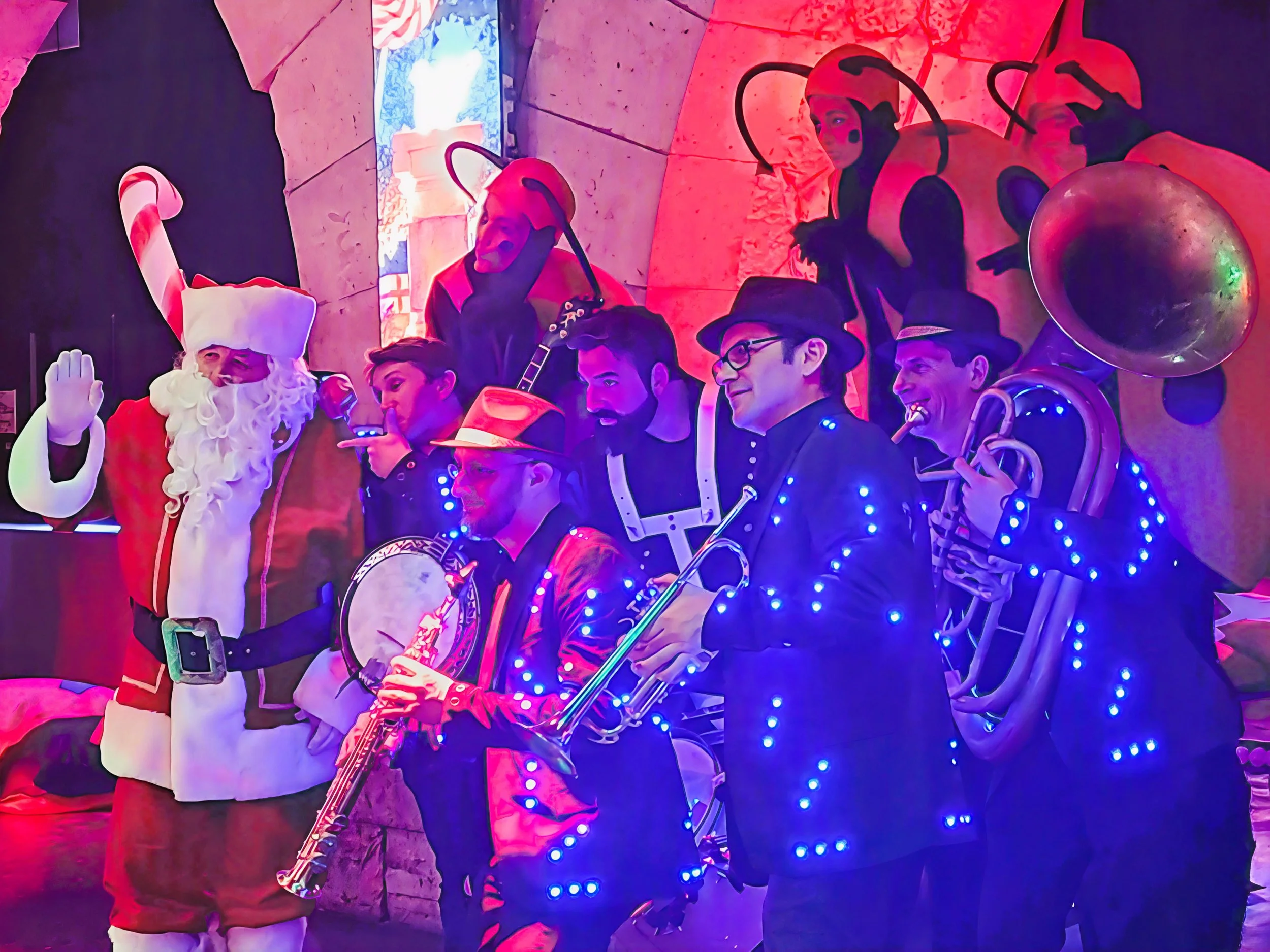 Un groupe de personnes déguisées en lutins de Noël et cowboys, avec des costumes illuminés par des lumières LED, posant dans un décor festif.