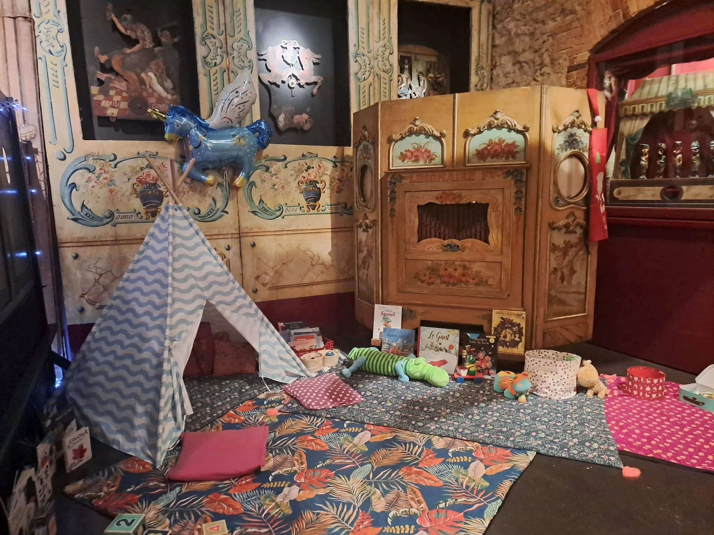 Une scène intérieure de marché ou de boutique avec des jouets, livres, coussins, et décorations, ainsi qu'une tente en tissu à motif floral.