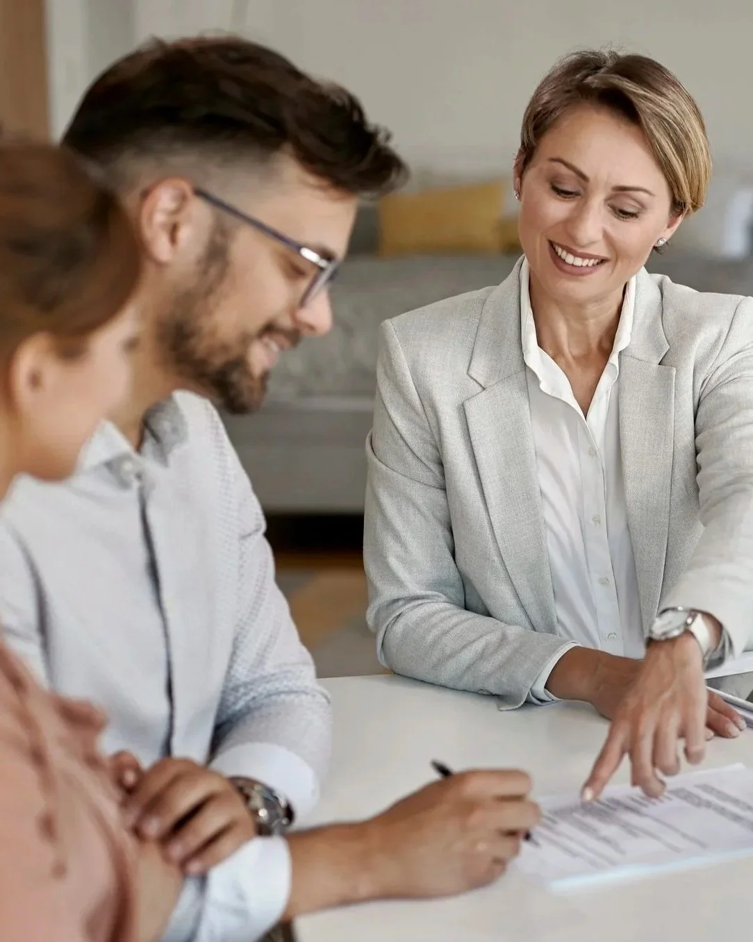 Three professionals in a meeting, two women and one man, discussing documents on a table in an office.