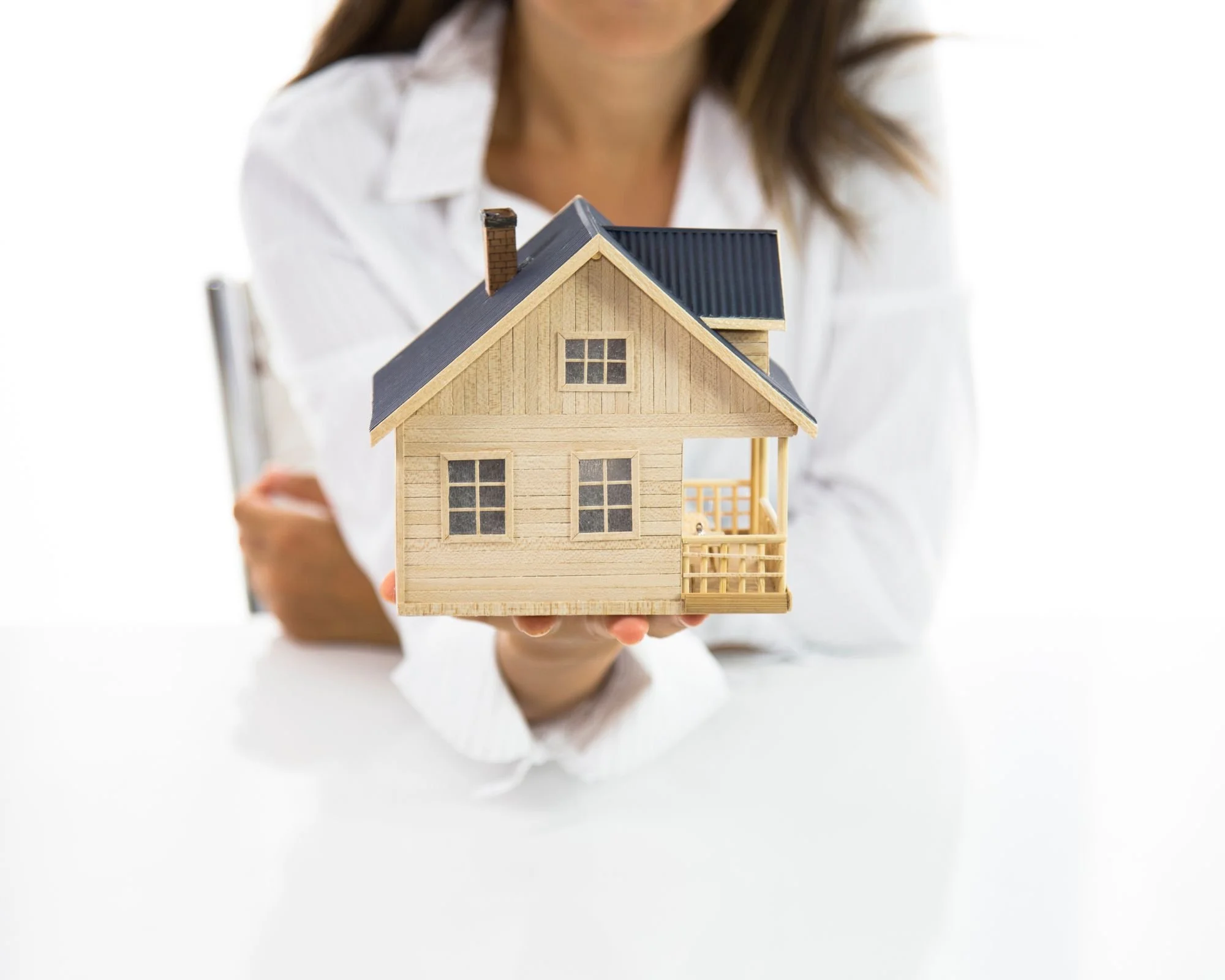 Person holding a detailed miniature wooden house model with a black roof and chimney, dressed in a white shirt.