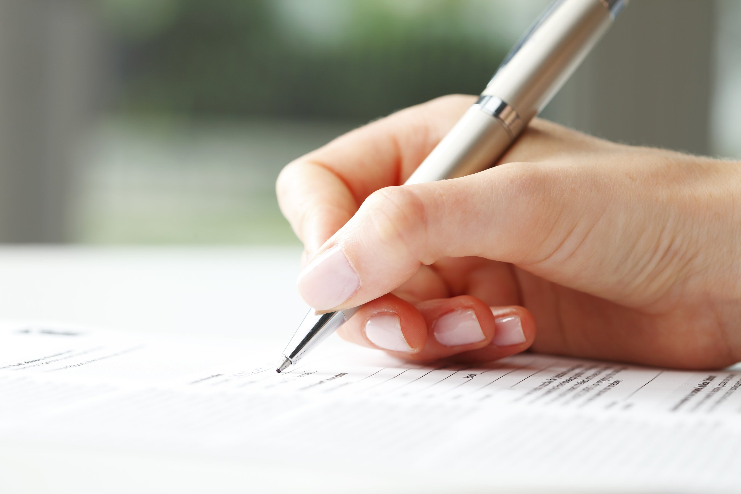 Close-up of a hand holding a silver pen writing on a document with printed text.