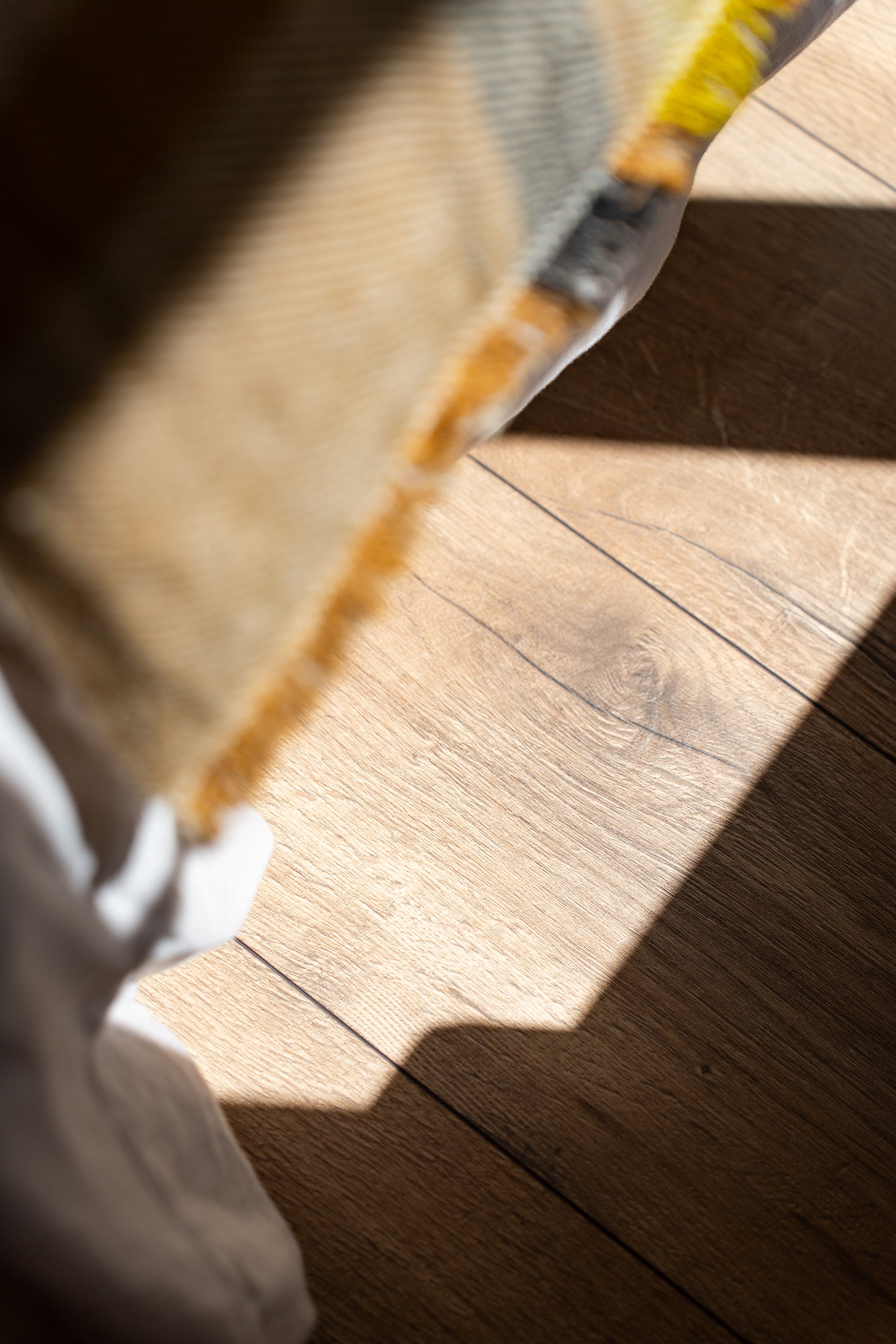 Vue d'angle d'une chaussure de sport blanche et beige sur un sol en bois, avec ombre projetée.