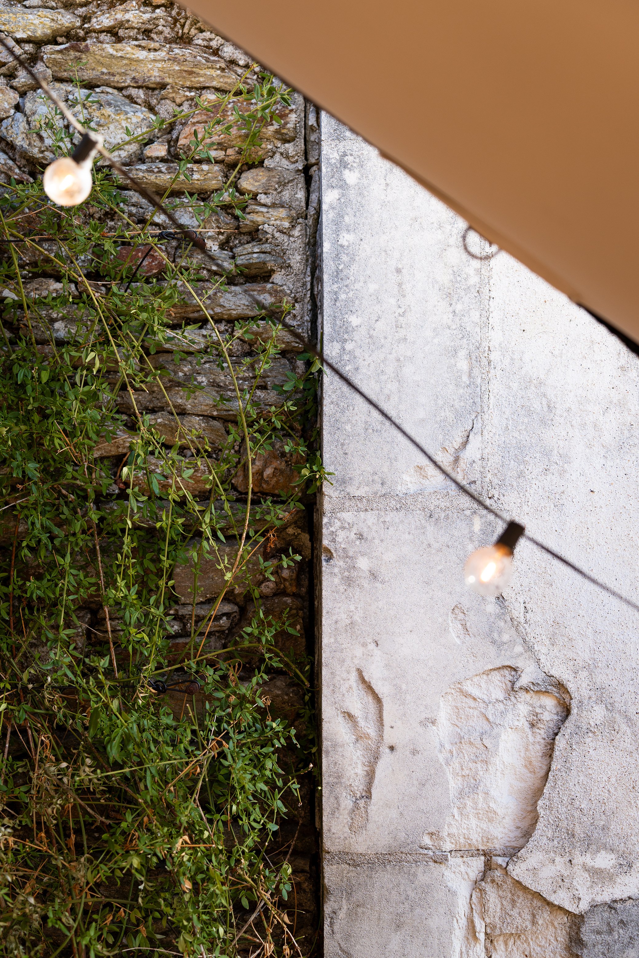 Mur en pierre jonché de végétation à gauche, mur en béton usé à droite, éclairage de Noël suspendu au-dessus.