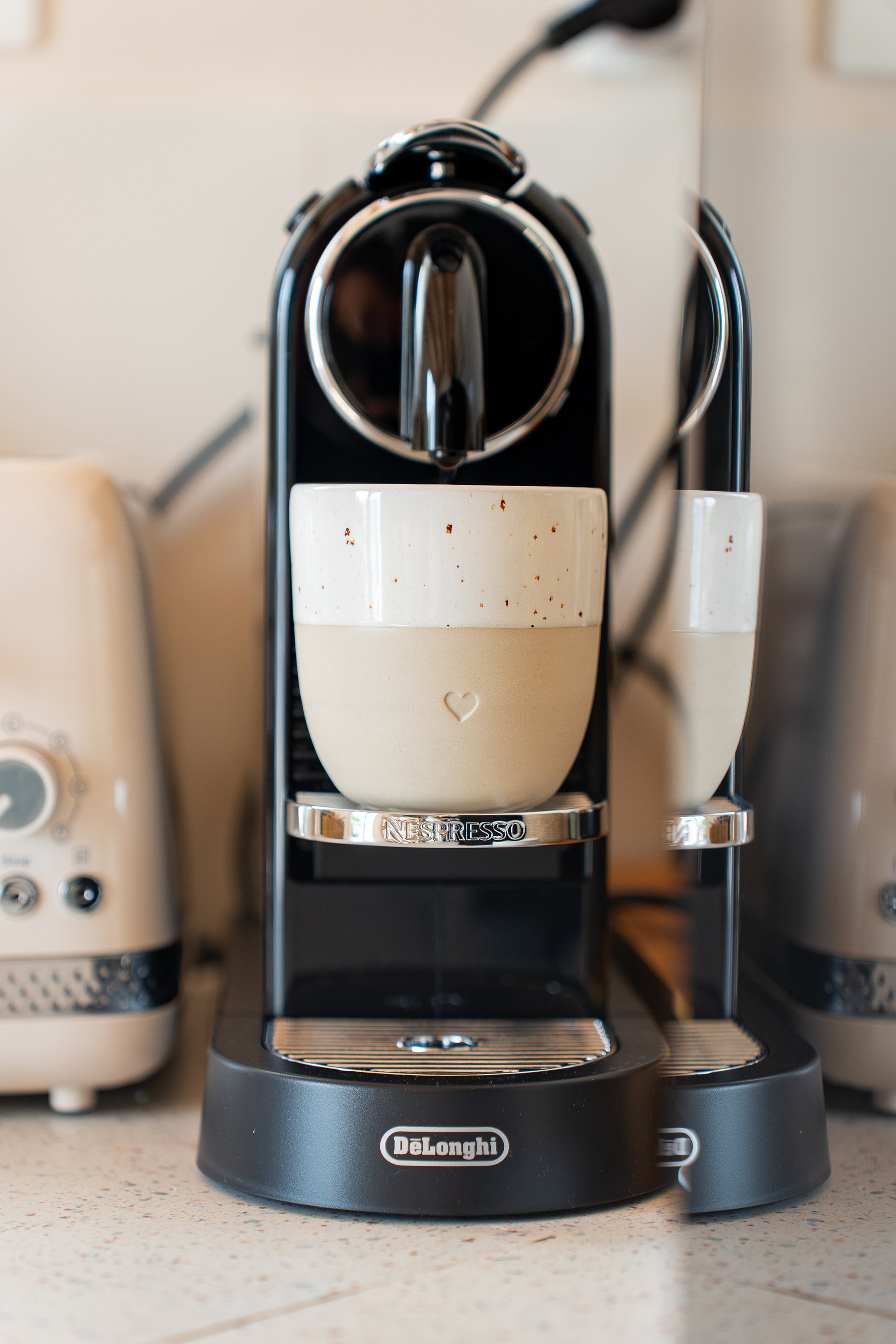 Une machine à café Nespresso DeLonghi noire avec une tasse en dessous, sur un comptoir de cuisine.