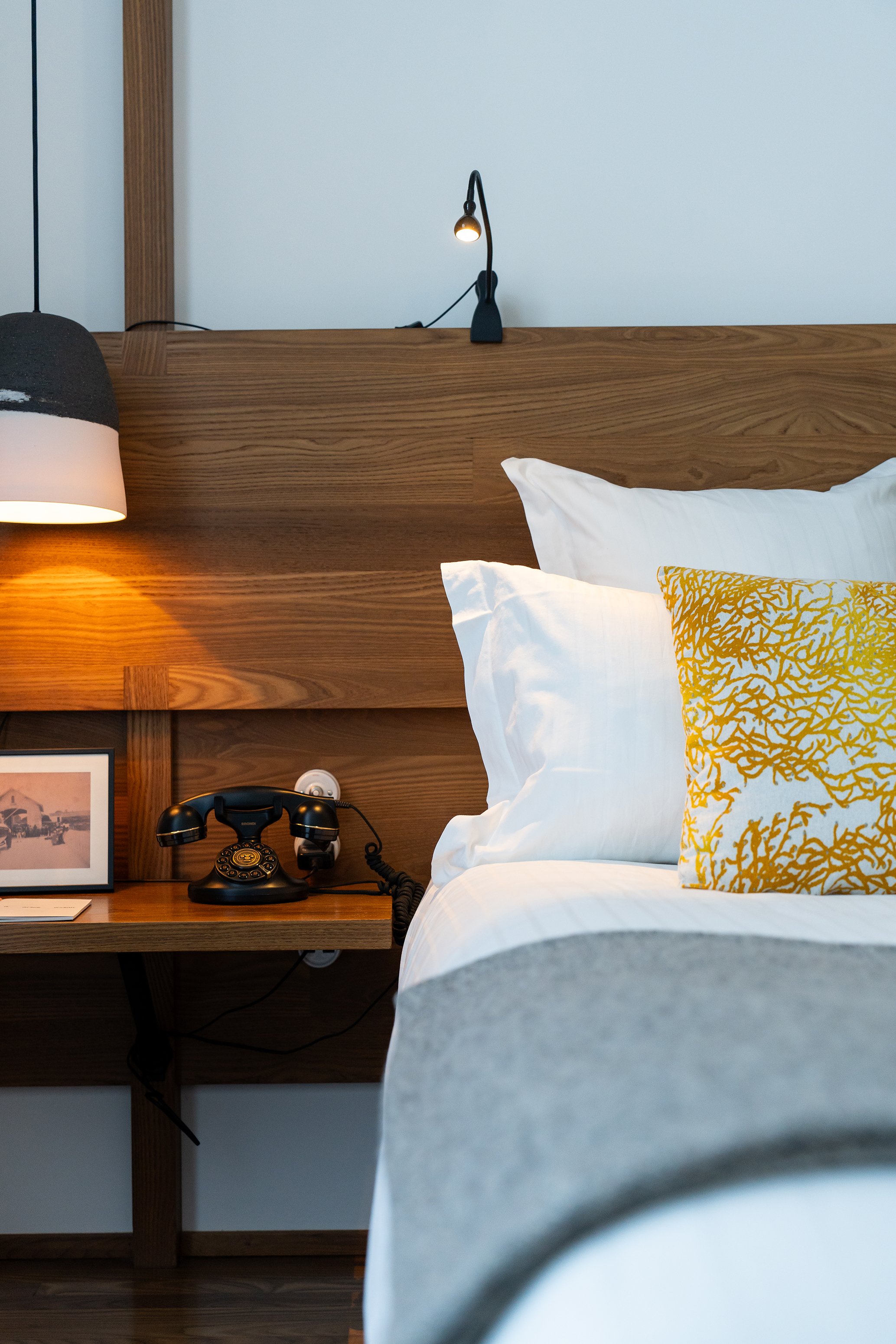 Un lit dans une chambre avec une tête de lit en bois, une lampe de lecture, un téléphone vintage sur une table de chevet et une décoration élégante.