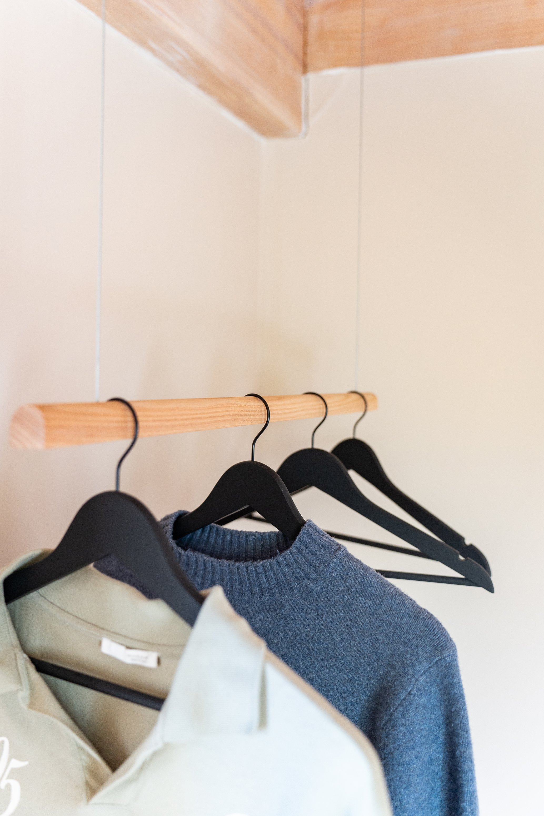 Vêtements suspendus sur des cintres noirs accrochés à une tringle en bois, dans une armoire ou un dressing.