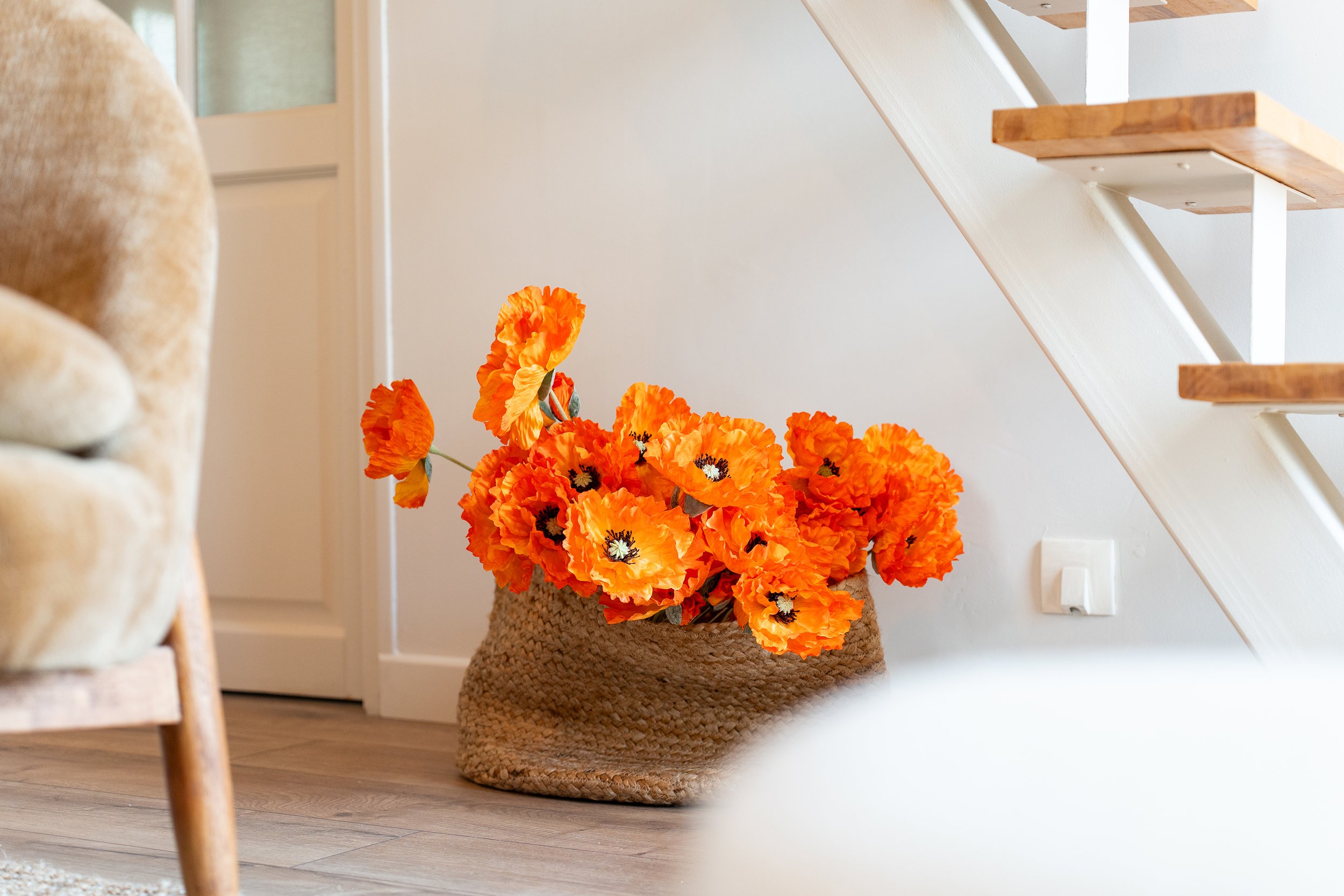 Un panier en osier rempli de fleurs orange éclatantes à côté d'une échelle en bois dans une pièce lumineuse.