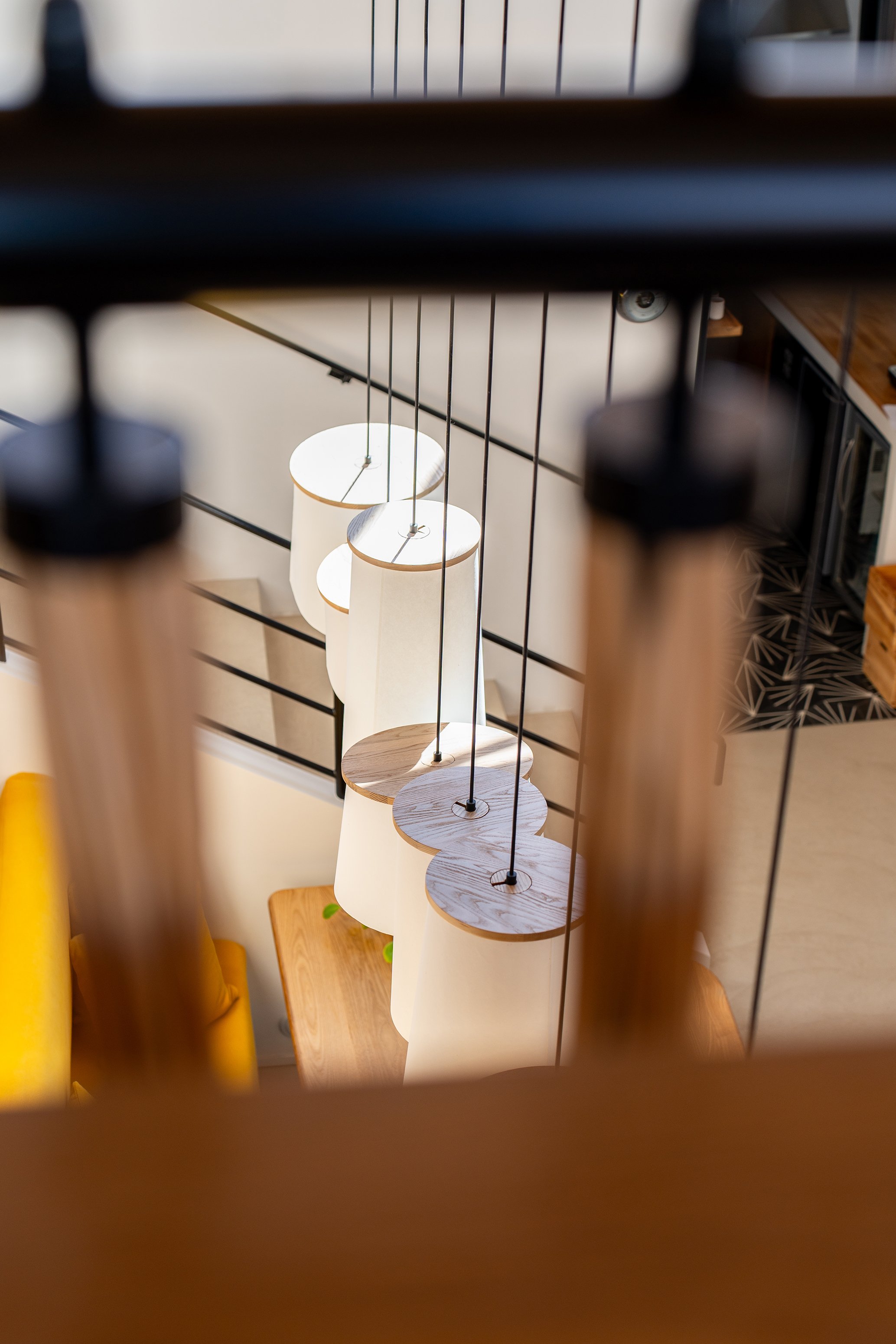 L'image montre une série de lampes suspendues en ligne, vues à travers une structure en métal, avec un intérieur moderne.