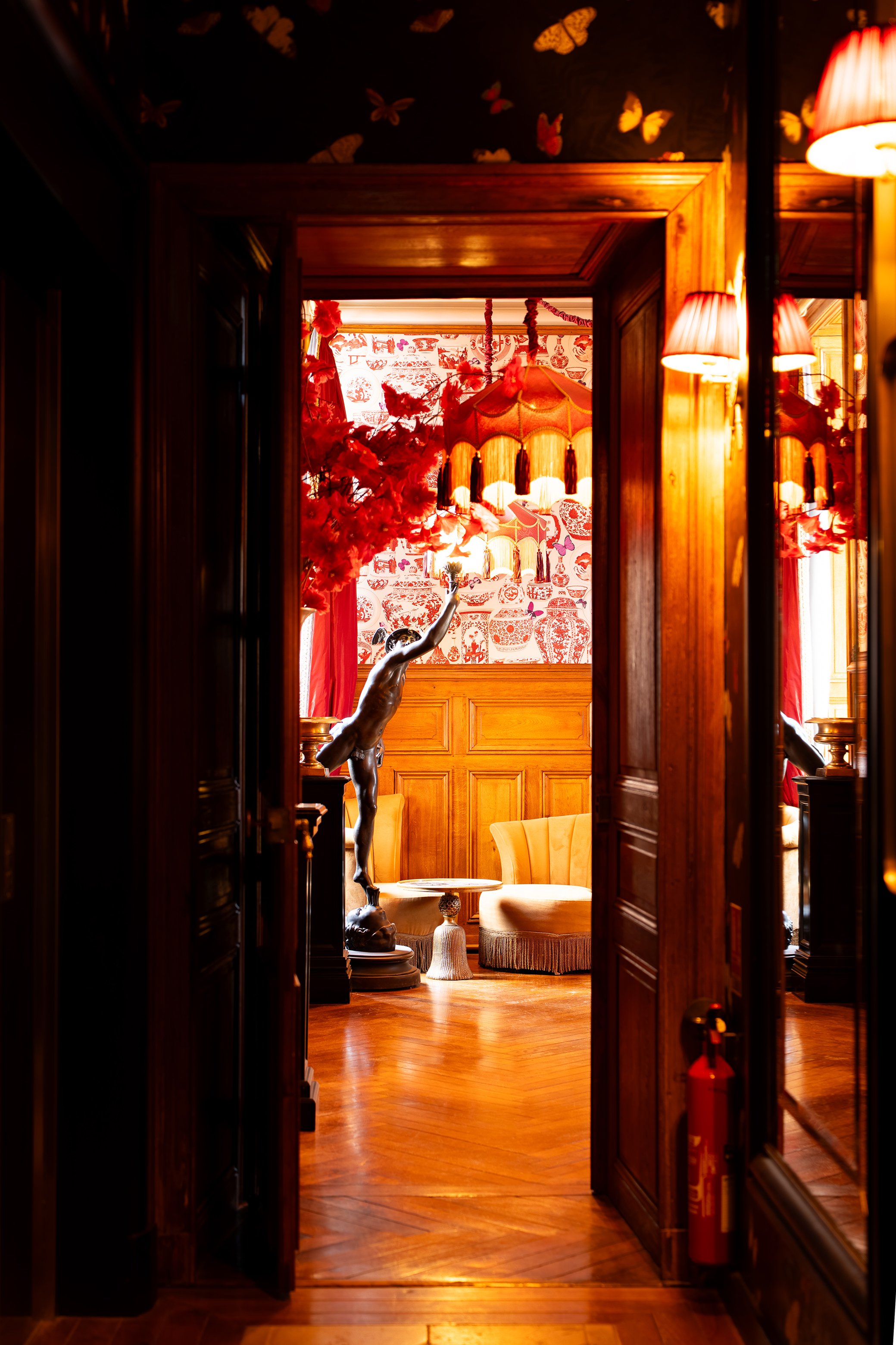 Une salle d'intérieur chaleureuse avec mobilier en bois, un éclairage tamisé, un lampadaire rouge, des décorations florales et une fresque murale rouge et blanche.