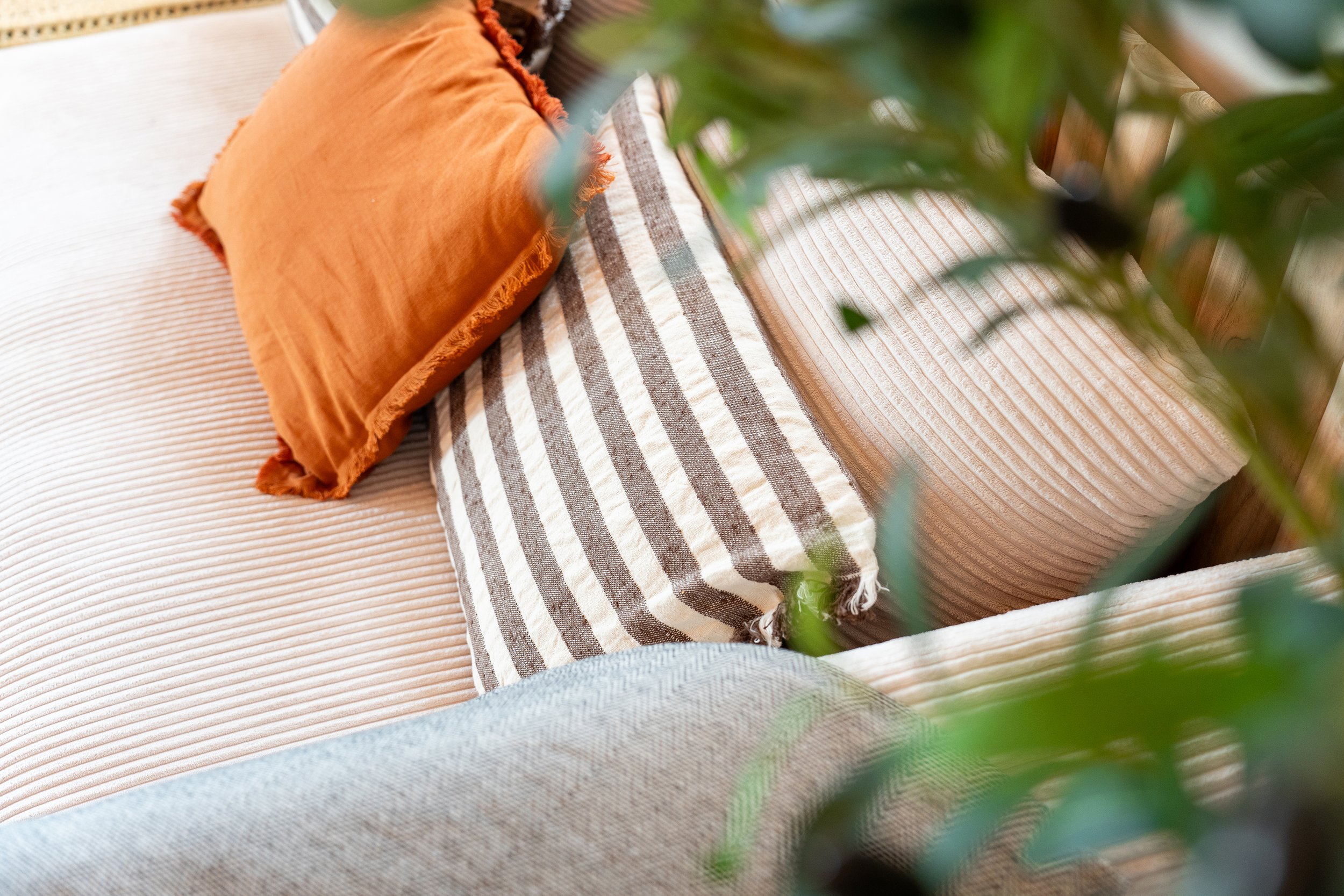 Coussins en tissu orange et beige avec rayures, posés sur un canapé à motif en maille.