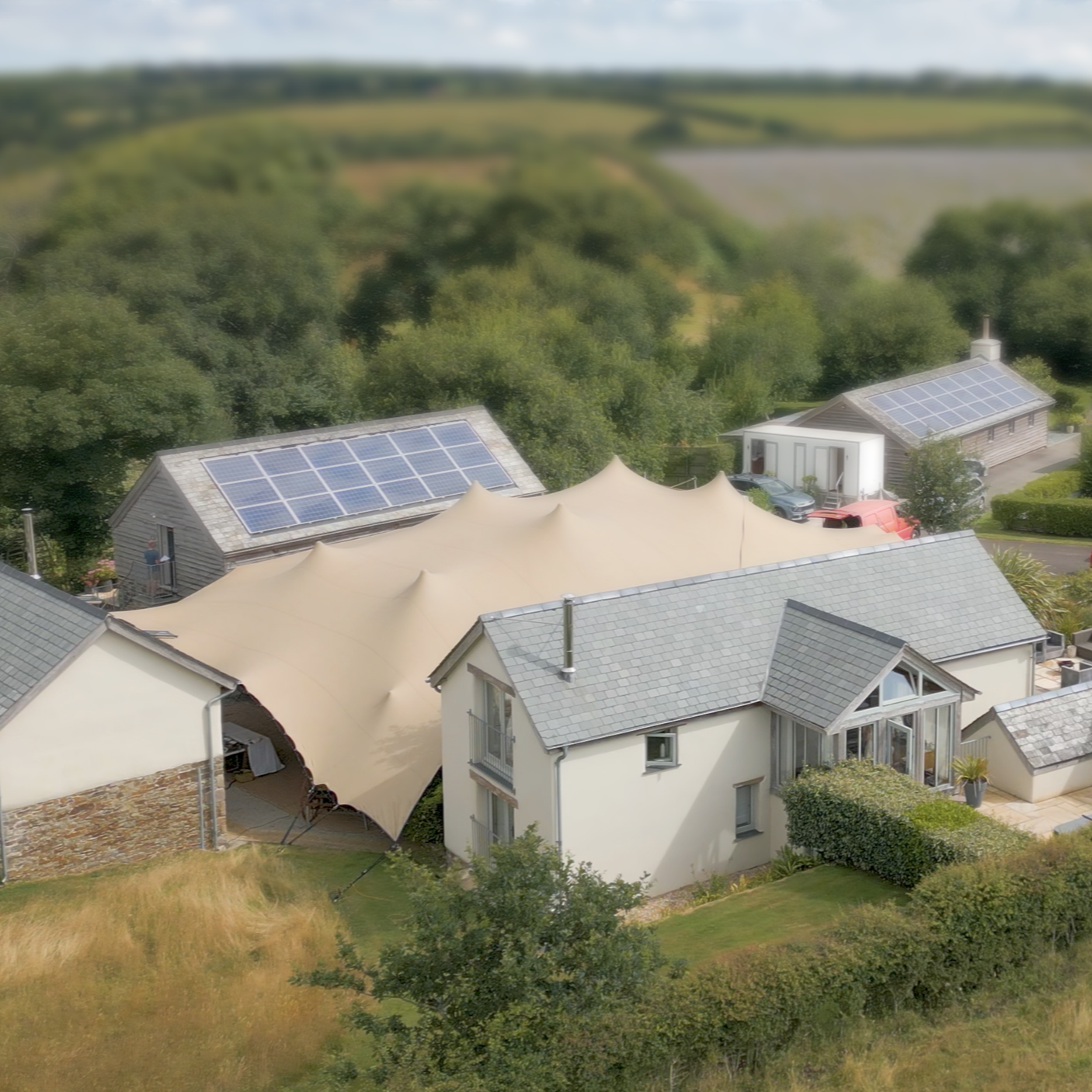 A residential area with houses featuring solar panels on their roofs, surrounded by greenery and distant fields.