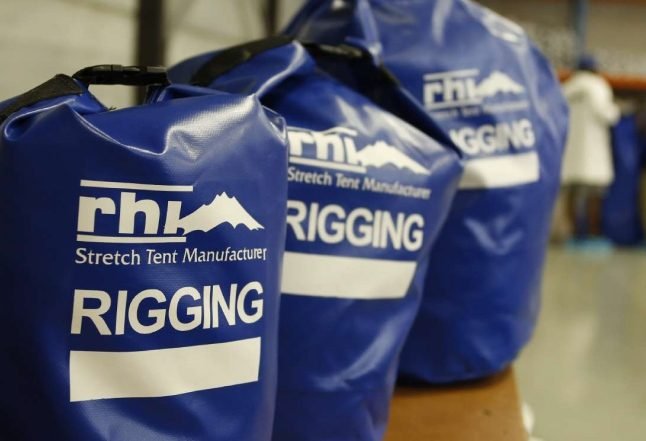 Blue bags labeled 'rhw Stretch Tent Manufacturer RIGGING' on a table in a workshop.