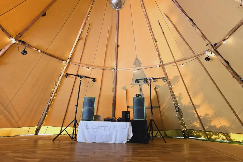 Interior of a tipi tent set up for a party or event, with a DJ booth, speakers, and lighting equipment arranged at the front.