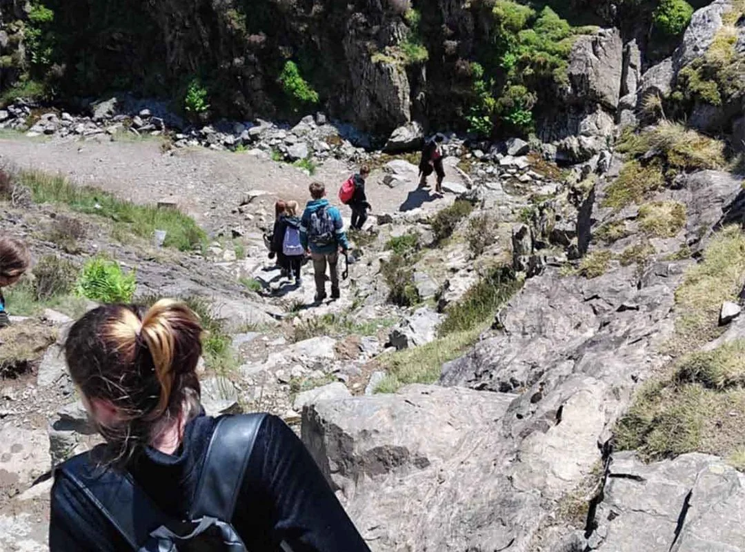 A group of hikers walking along a rocky trail in a mountainous area with steep cliffs and sparse vegetation.