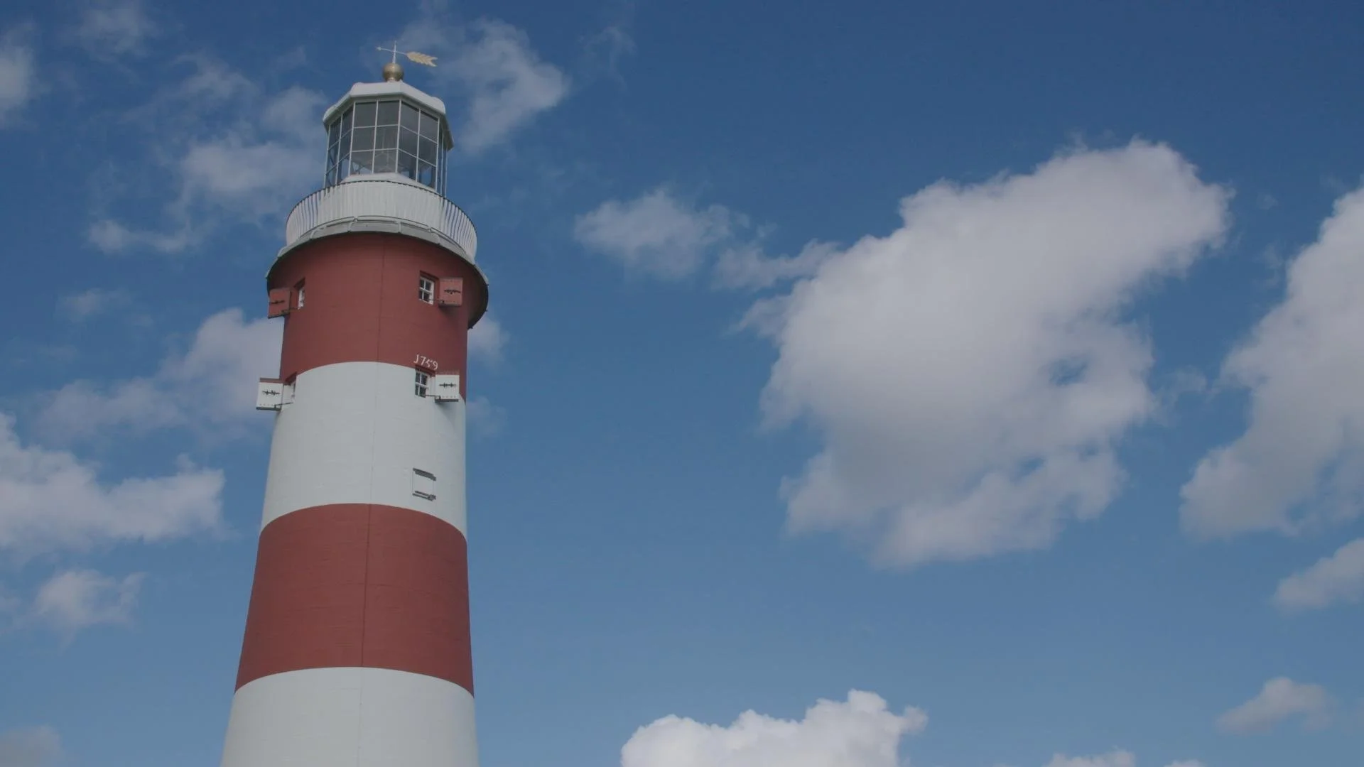 A red and white striped lighthouse with blue sky and scattered clouds in the background.